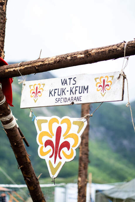 Bilde av enkelt gruppeskilt der navn og logo er malt på en plankebit.